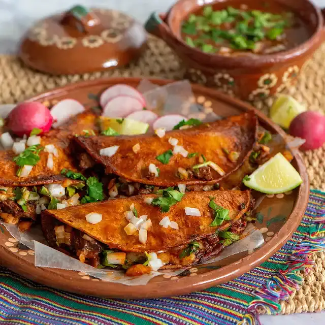 A plate of tacos coated in red chile sauce and filled with beef