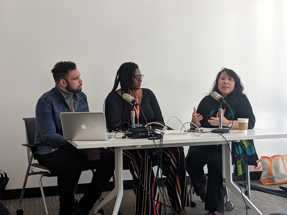 Three people sit at a table, speaking into microphones.