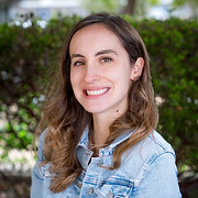 Smiling woman poses in front of greenery background. 