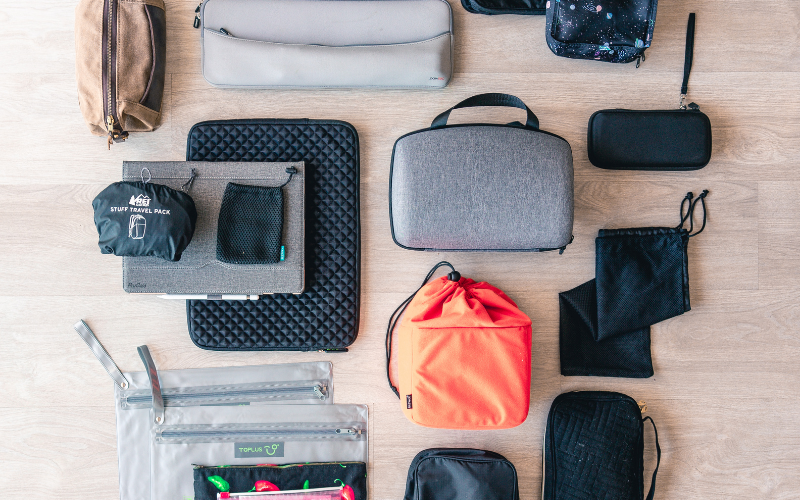 Flat-lay of travel packing cubes, pouches, and organisers arranged on a wooden floor
