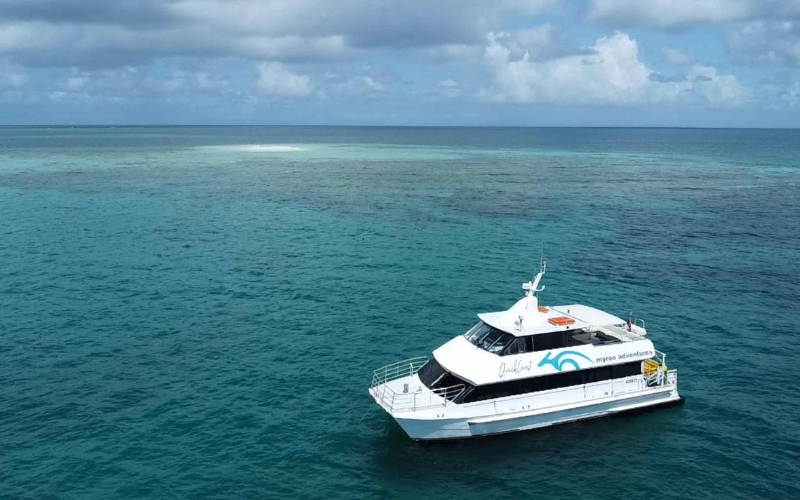 A tour boat sailing on calm turquoise waters at the Great Barrier Reef during the dry season