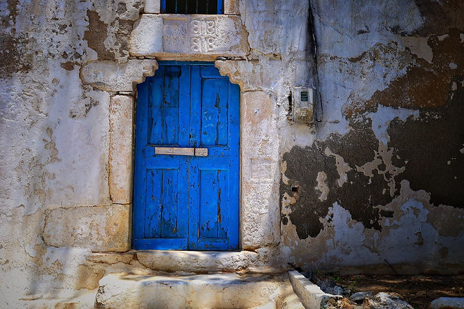 Steinstufe zu einer blauen Holztüre umgeben von altem Gemäuer.