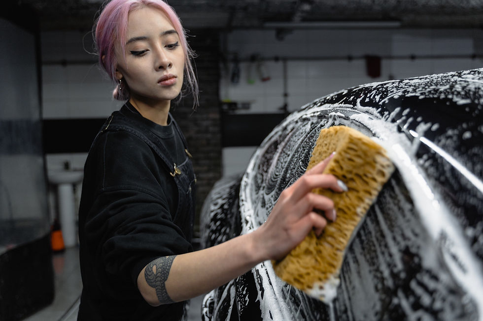 Asian woman in black outfit washing car with large brown sponge