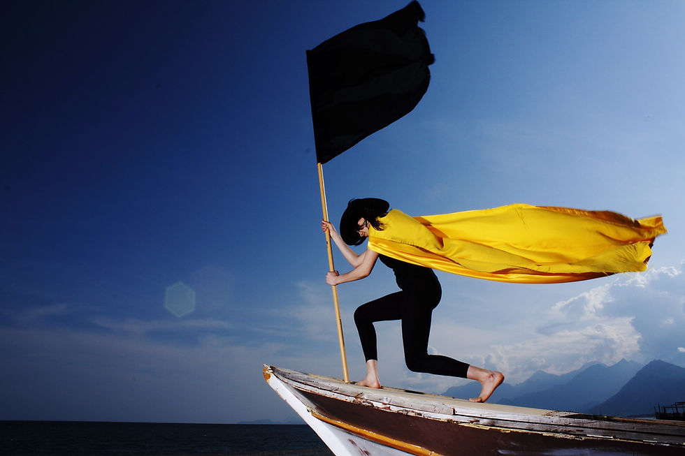 Woman in black outfit with black hat, holding a black flag, planting it in a yellow cape
