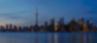 Toronto skyline at evening with illuminated skyscrapers and CN Tower, reflecting on calm water.