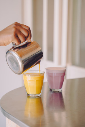 Hand pouring golden milk in a glass, next to a beetroot latte at kumi cafe in oslo