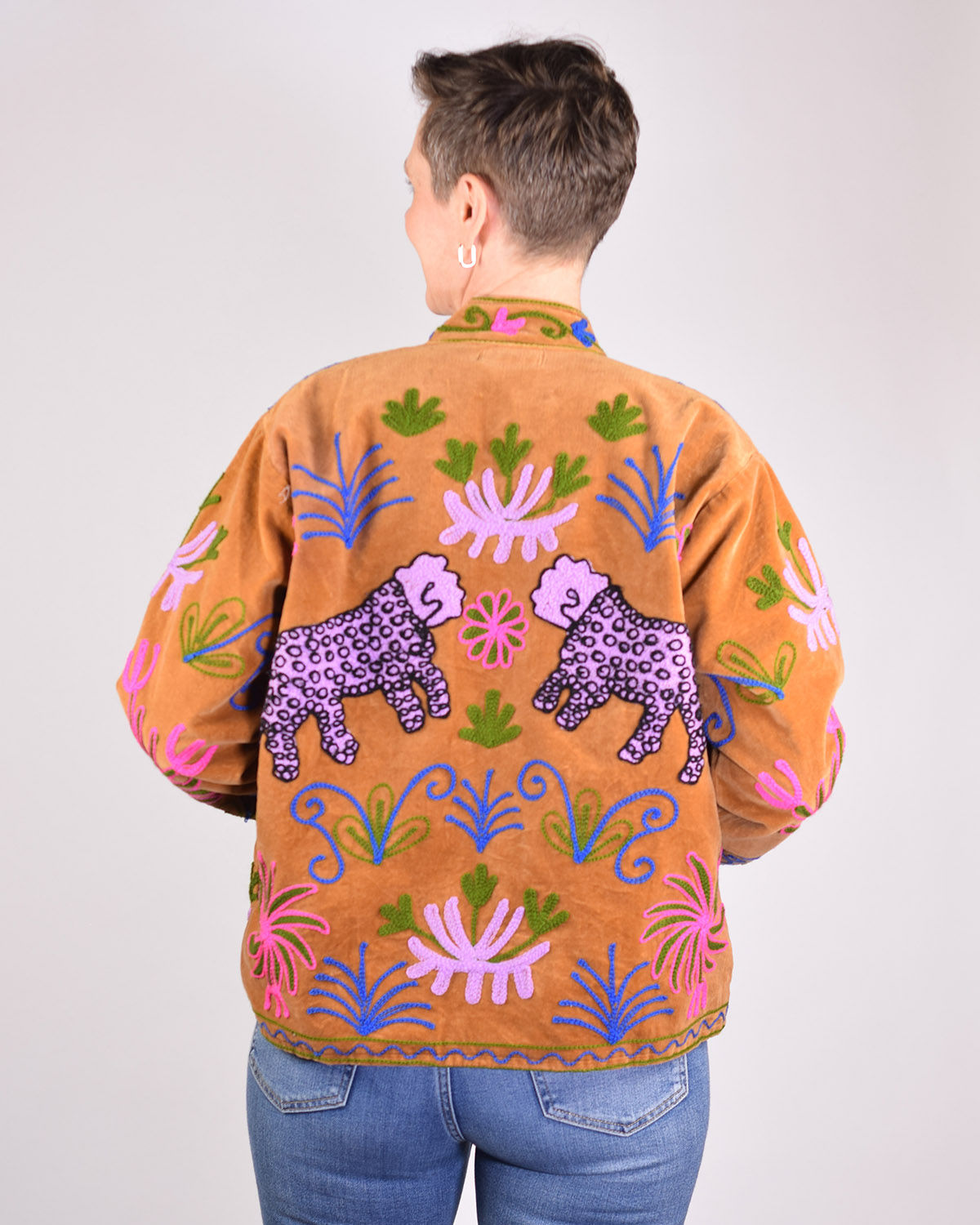 person wearing tan velvet jacket with purple leopards embroidered on the back - back view