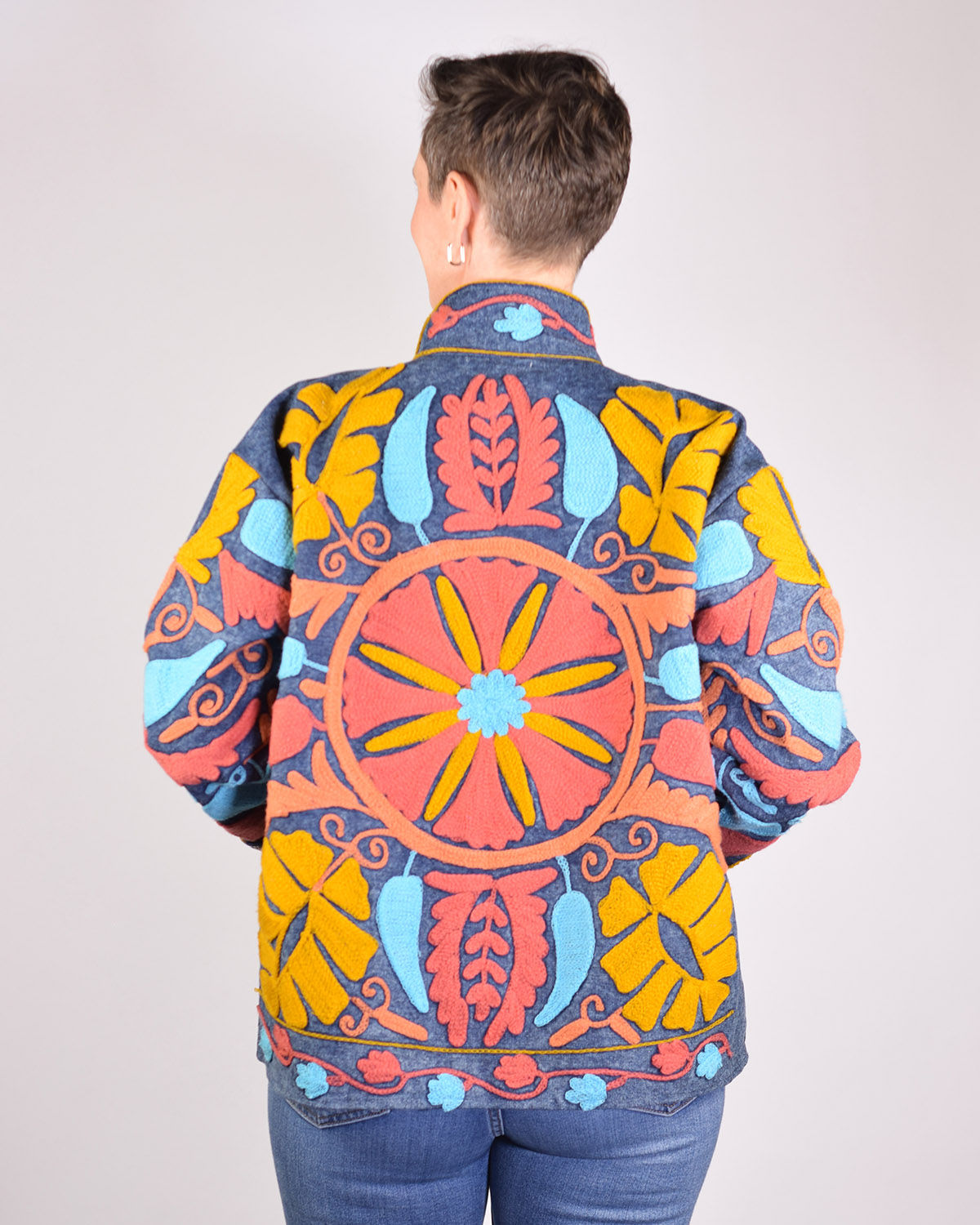 Person wearing a denim jacket covered in colorful embroidery - back view