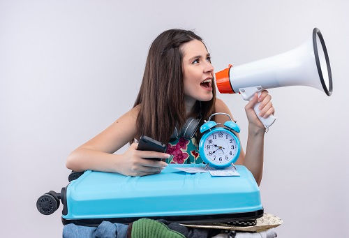 young-caucasian-traveler-girl-holding-mobile-phone-speaker-with-alarm-clock-suitcase-isola