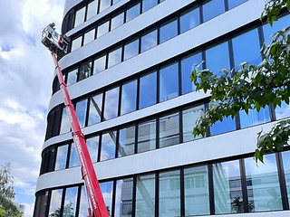 Mitarbeiter sitzt in einem ausgefahrenen Krankkorb, um die Fassadeund die Fenster eines hohen Gebäudes zu reinigen.