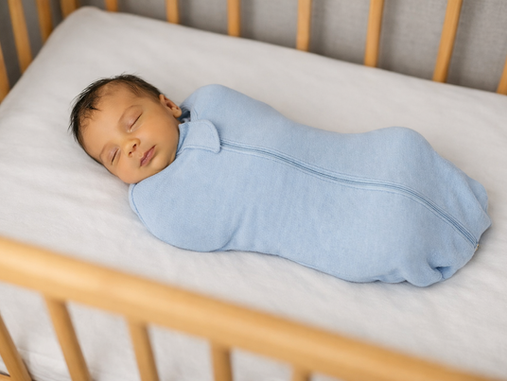 Sleeping newborn swaddled in light blue in a wooden crib with white bedding, peaceful and cozy.