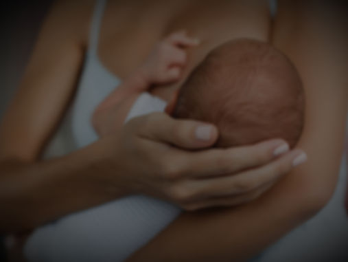 Close-up of a mother cradling a newborn baby against her chest, softly lit and tenderly intimate