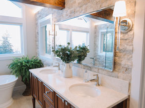 Timeless Tuscan-inspired primary bathroom remodel featuring a freestanding soaking tub, floor-to-ceiling stone walls, exposed wood beam, and custom cherry vanity.