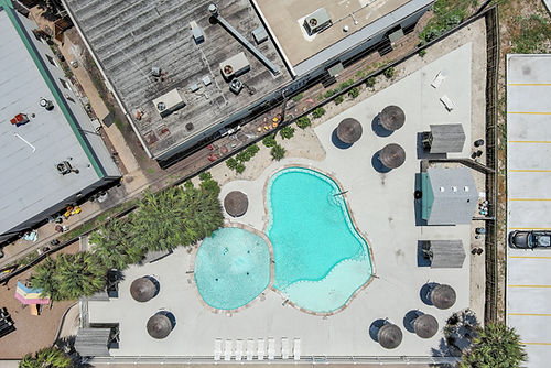 Aerial view of a turquoise pool surrounded with umbrellas and buildings STexasPhotography