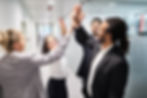 A group of colleagues joyfully giving a team high five in a bright, contemporary office space