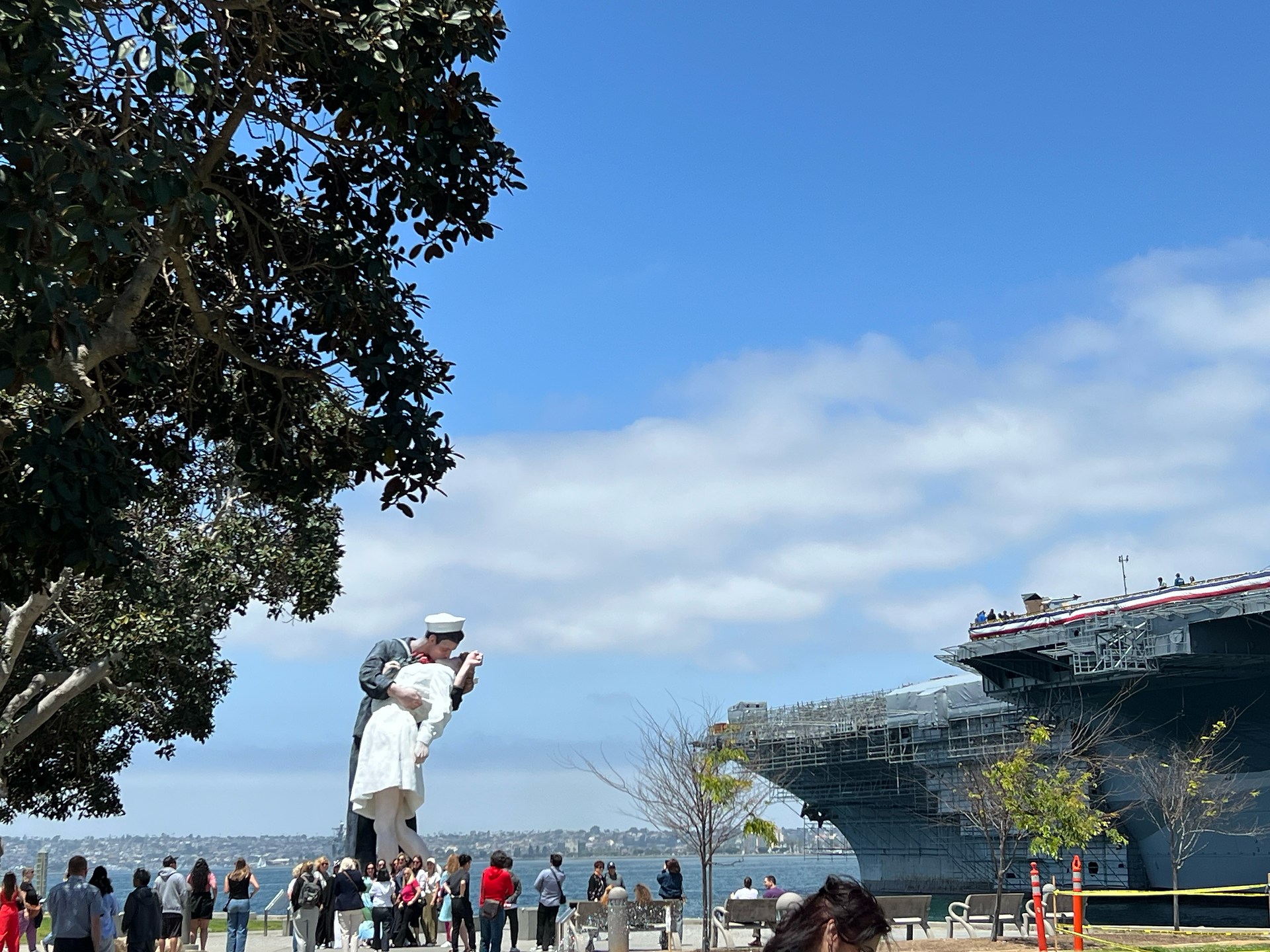The towering Unconditional Surrender kiss statue rising over visitors on the San Diego Embarcadero near the USS Midway.