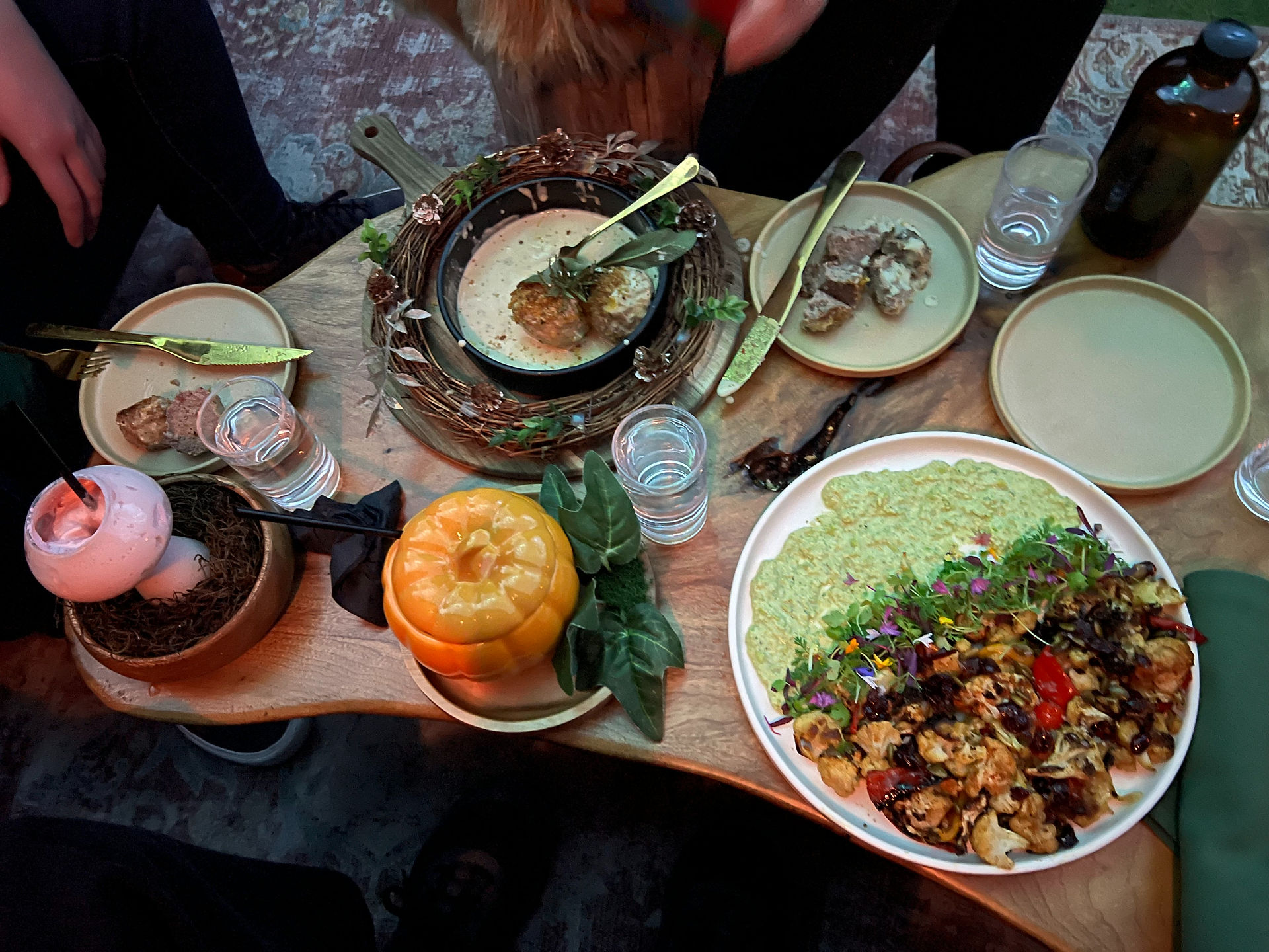 Top-down view of a whimsical table setting at Ember Lounge Desert Ridge, showcasing creatively presented cocktails, a meatball skillet in a rustic cast-iron dish, and colorful roasted cauliflower with edamame.