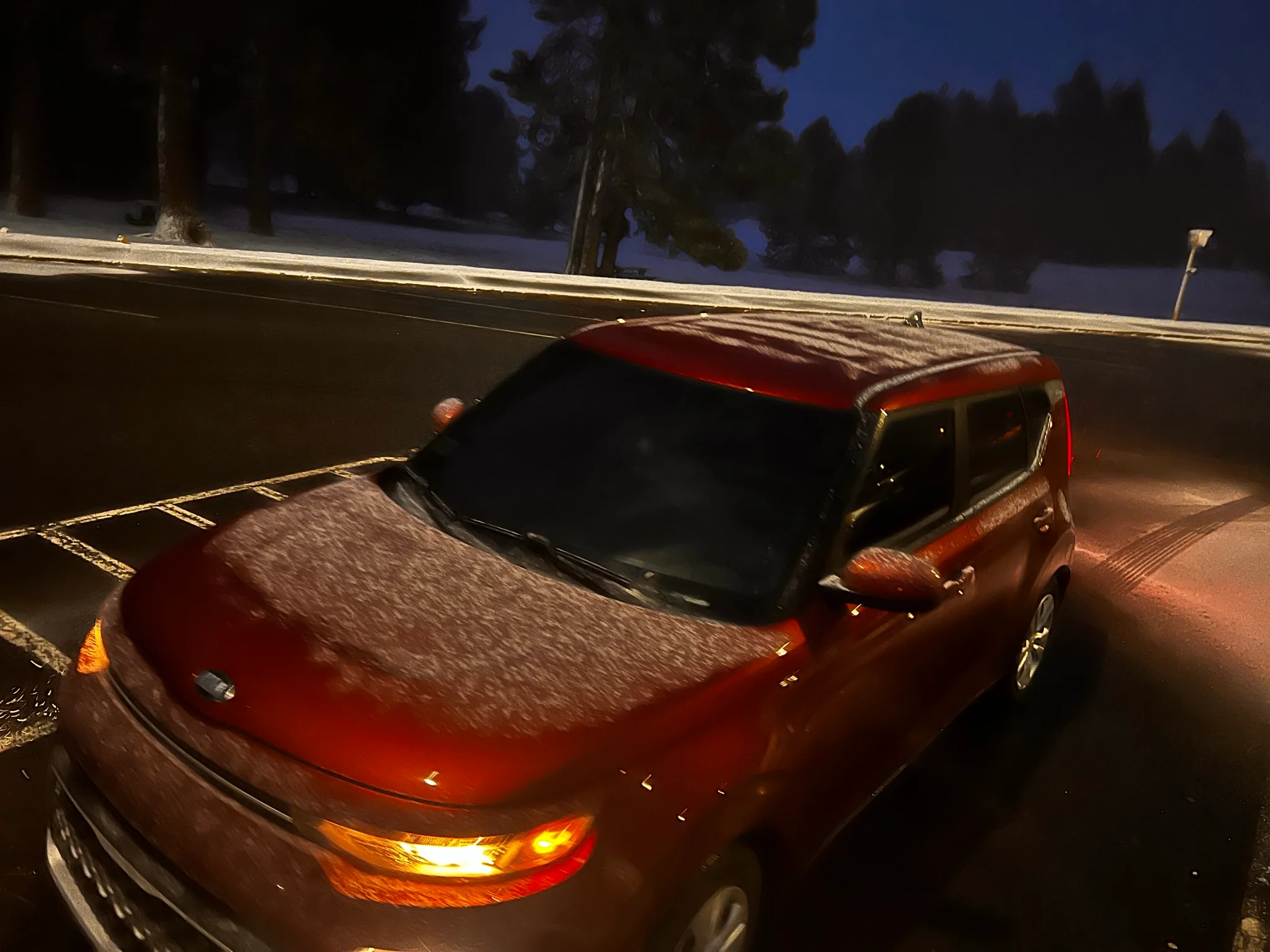 Orange Kia Soul with a light layer of snow in it in a parking lot. 