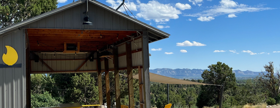Covered picnic area with yellow tables and chairs at Lake Pueblo State Park, offering a panoramic view of the surrounding mountains and forest. The sky is clear with a few scattered clouds, adding to the scenic and inviting atmosphere.