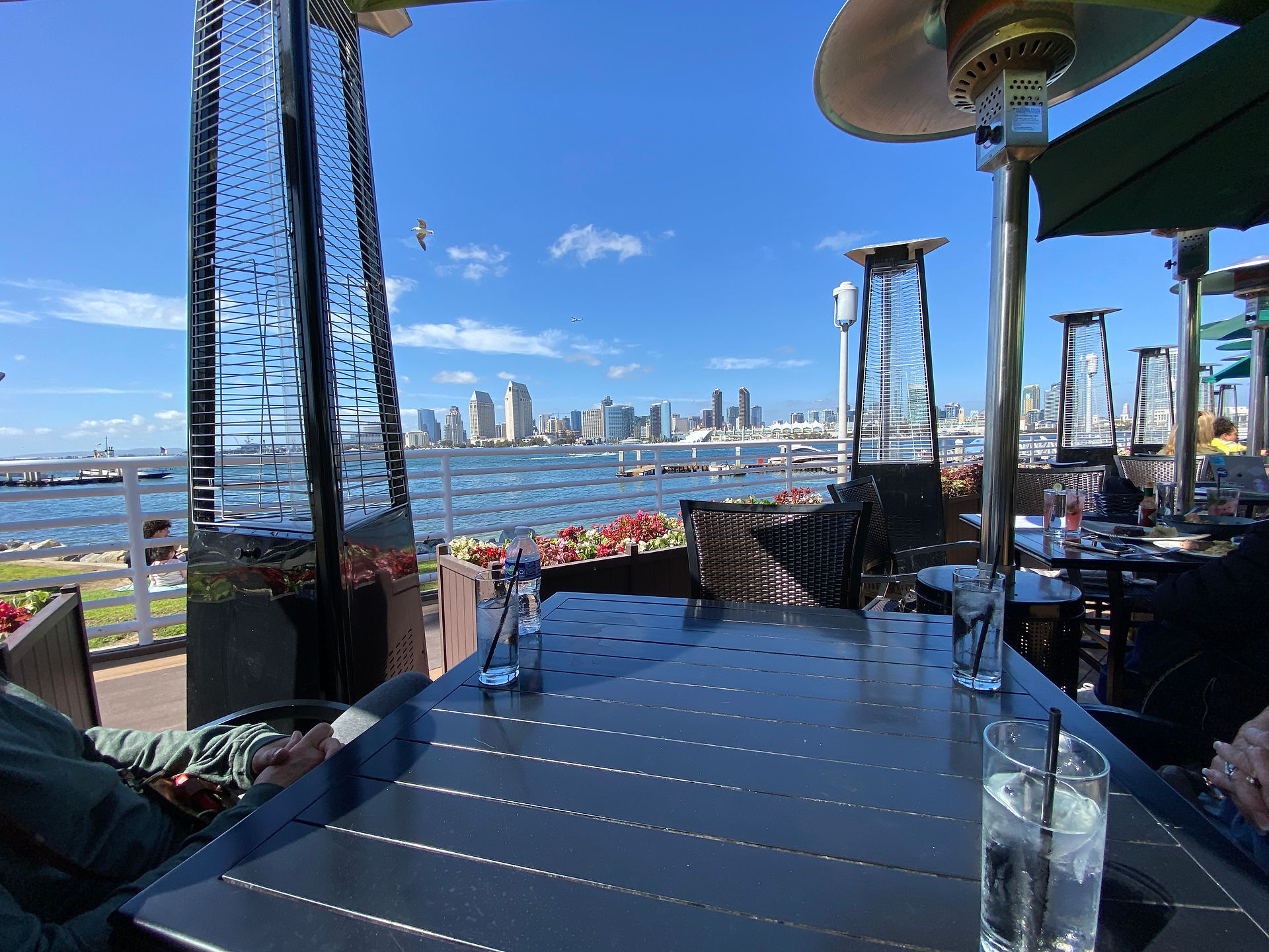 Waterfront restaurant patio with heat lamps overlooking the San Diego skyline across the bay.