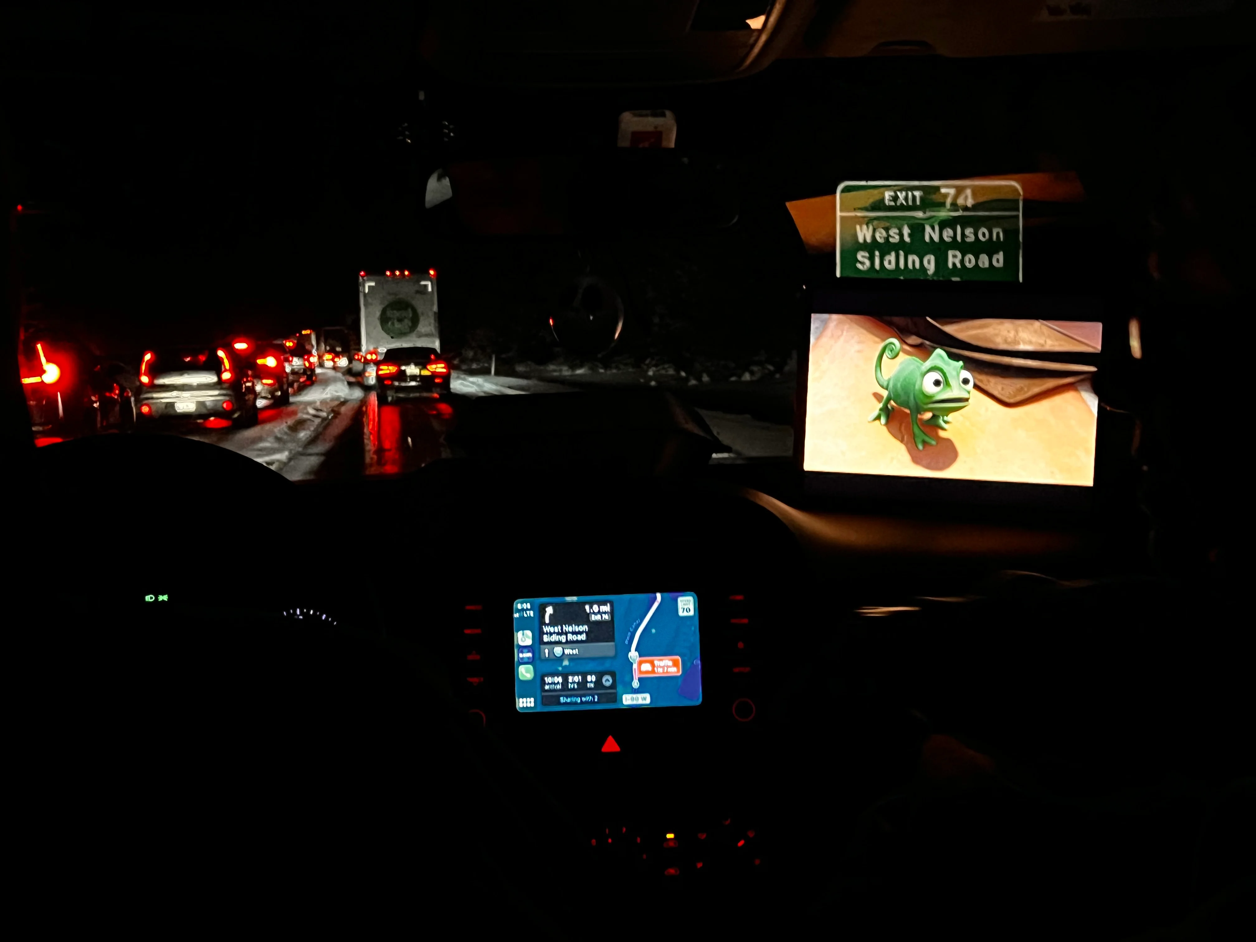 Inside a car looking on to stopped traffic on a highway at night during a snow storm.