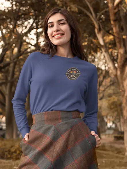 A lady in the woods wearing a blue long sleeve tee and a plaid skirt. 
