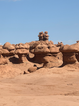 Cluster of mushroom-shaped red sandstone formations at Goblin Valley State Park in Utah, standing against a clear blue sky and desert landscape.