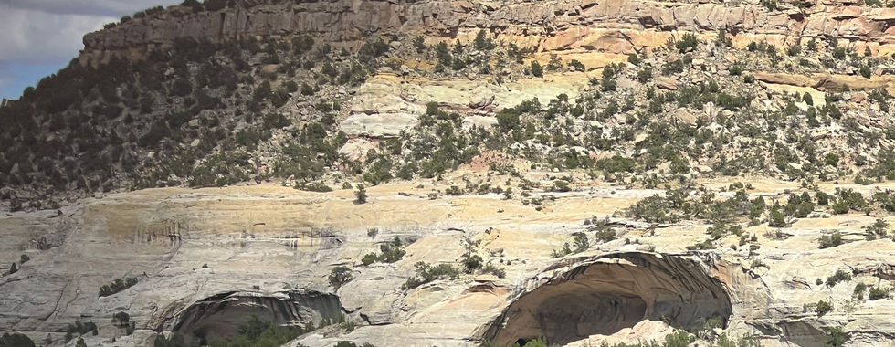 A view of a rugged hill with several large caves in the rocky face, surrounded by sparse vegetation and under a partly cloudy sky."