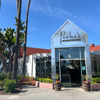 Entrance to Peohe’s restaurant at Coronado Ferry Landing, featuring a modern glass façade, palm trees, and landscaped greenery under a clear blue sky.