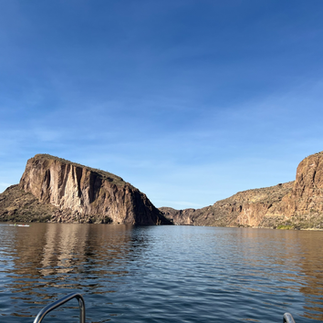 Wide view of Canyon Lake with smooth reflective water, surrounded by large rocky cliffs and a distinct flat-topped rock formation, all beneath a bright blue sky.