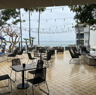 Covered outdoor patio lounge with bistro tables and string lights overlooking the bay at a Coronado resort.