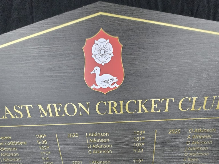Close-up of East Meon Cricket Club ACM honours board showing gold vinyl lettering, yearly records, and red club crest.