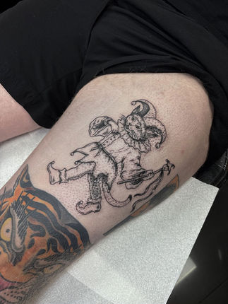 Fine line and dotwork thigh tattoo of a cat dressed as a jester, holding a sceptre.