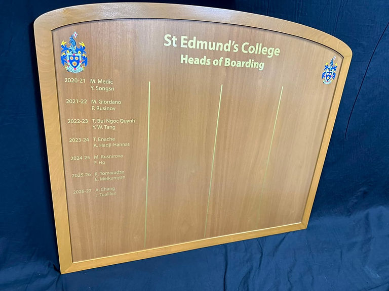 Close-up detail of St Edmund's College wooden honours board showing gold leaf names, year columns and painted college crest.