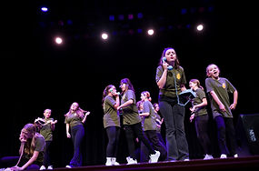A group of students onstage wearing green Ponderosa Players shirts and talking on vintage telephones.