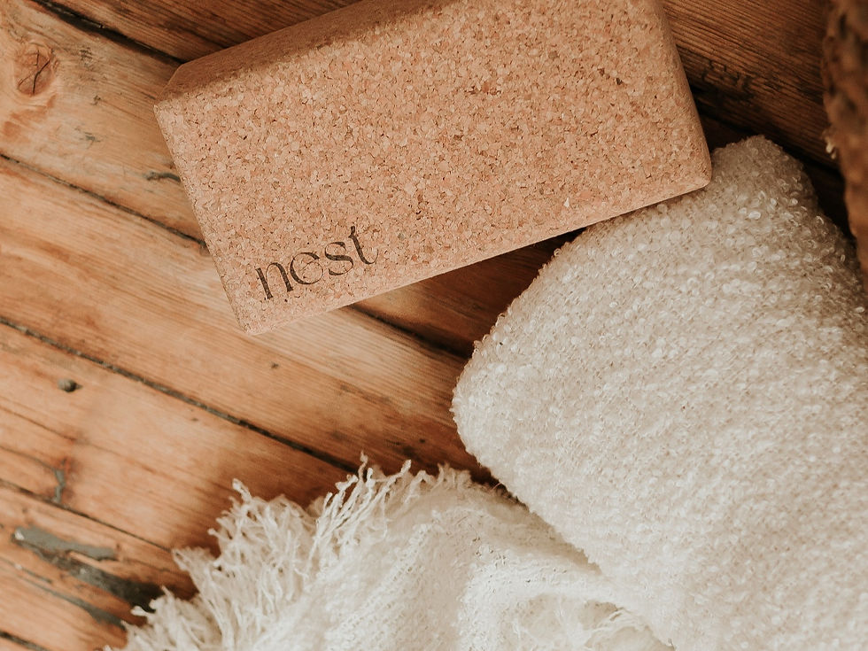 Cork yoga block labeled "nest" on wooden floor next to a white textured blanket, creating a cozy, natural setting.