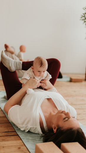 Mum lying on a yoga mat holding her baby during a gentle baby yoga session at Nest Glasgow.