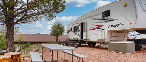 Picnic table and towering pine tree next to stationary RV rental for vacations at Highland Meadows with view of the Black Hills.