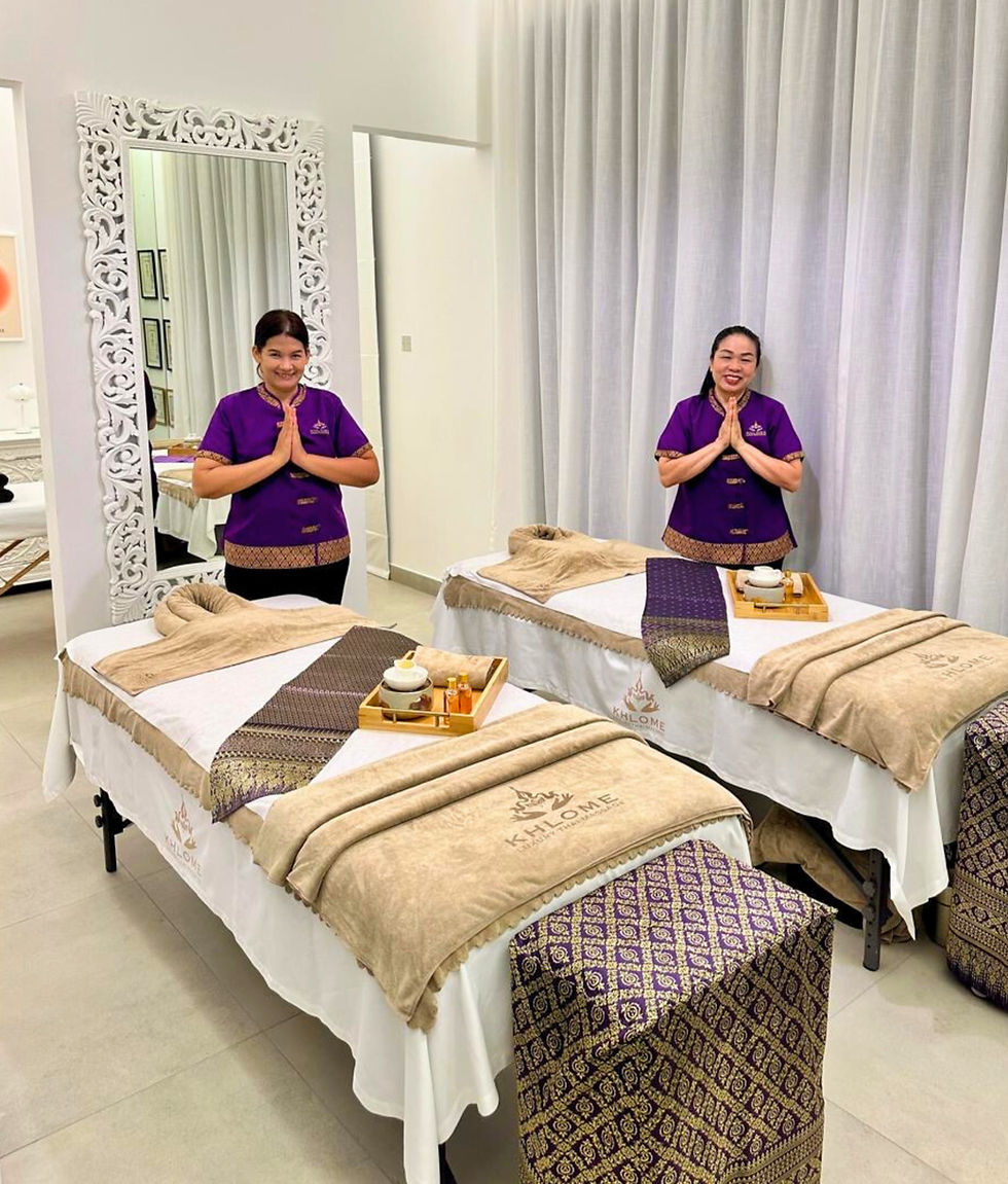 Two Thai massage therapists standing beside prepared massage beds in a home spa setup.