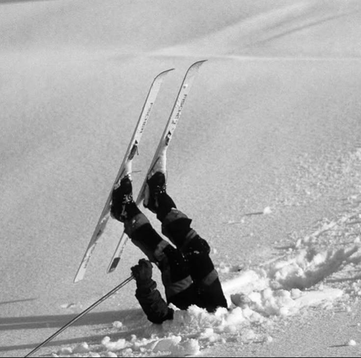Pessoa parcialmente submersa na neve, com pernas erguidas e esquis para cima.