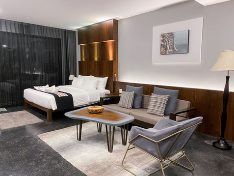 Nai Ya Hotel Premium Room has a living area consisting of a sofa and an arm chair next to the bed. The bed is at the far end near the large window which guest can walk out to the patio that can access the swimming pool.