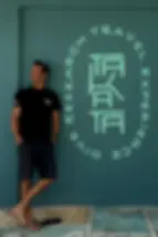 PADI Course Director Manlio Leggio standing aside the Takata Experience's logo painted on the diving shop wall.