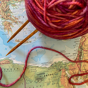 Pink yarn with knitting needles sticking out sits on top of a map showing Egypt and the Mediterranian Sea.