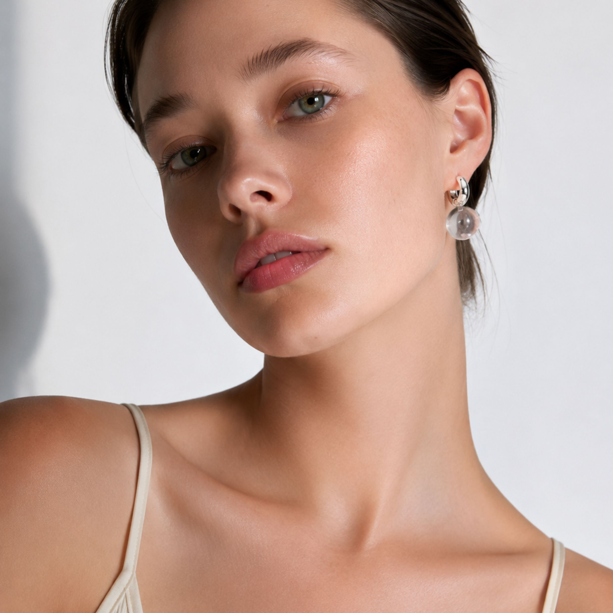 Model wearing Luna Crystal Sphere Drop Huggy Earrings with polished silver-tone hoops and clear resin sphere drops.