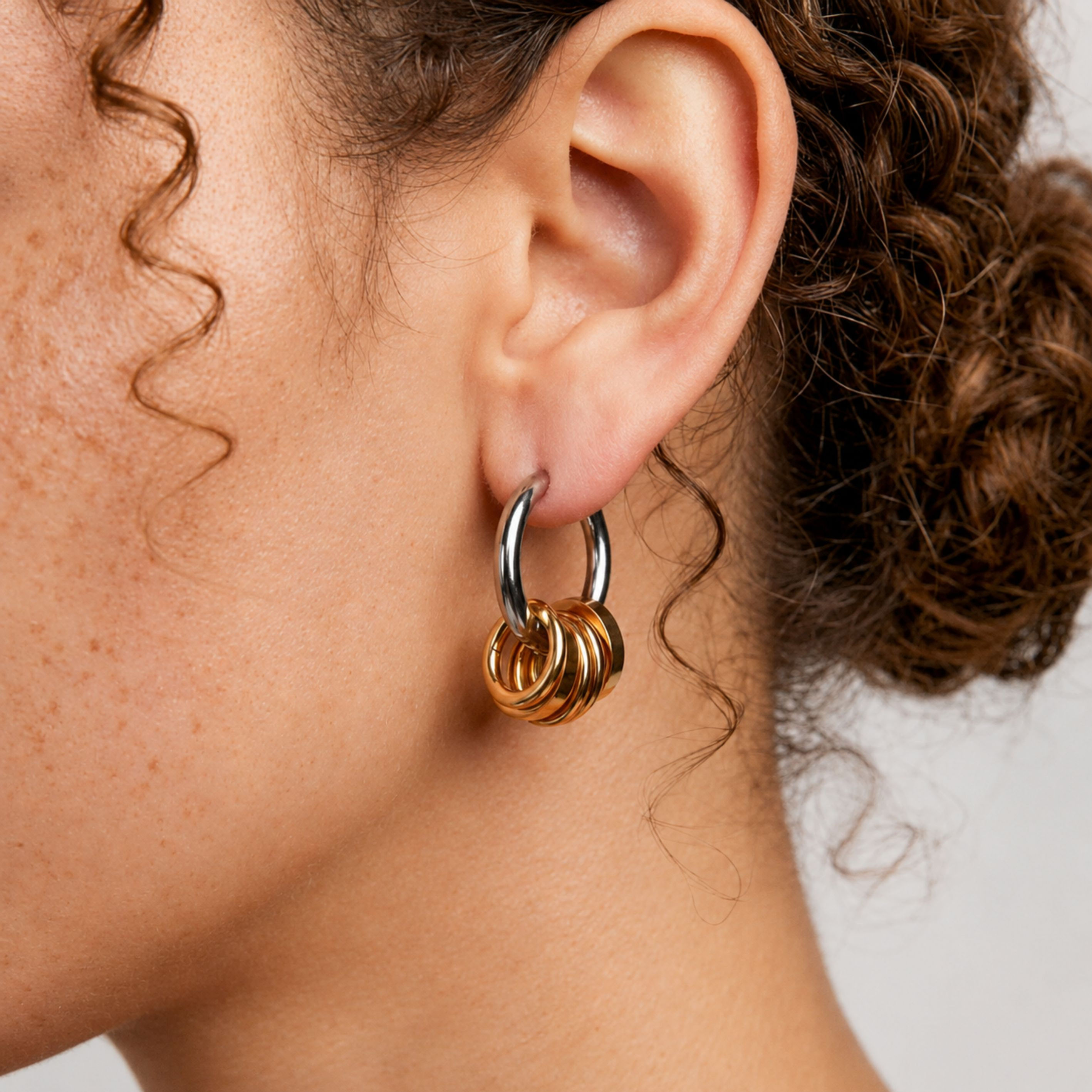 Side profile close-up of a model wearing Amara Mixed Metal Ring Hoop Earrings with stacked gold ring charms and silver hoops.
