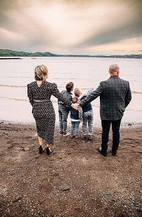 A family with their backs to the ocean gazing at the sunset. Mom and dad holding hands.