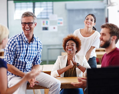 A group of diverse professionals in a casual office setting sharing laughter and collaboration, embodying leadership consulting, team building workshops, and creating a thriving workplace culture.