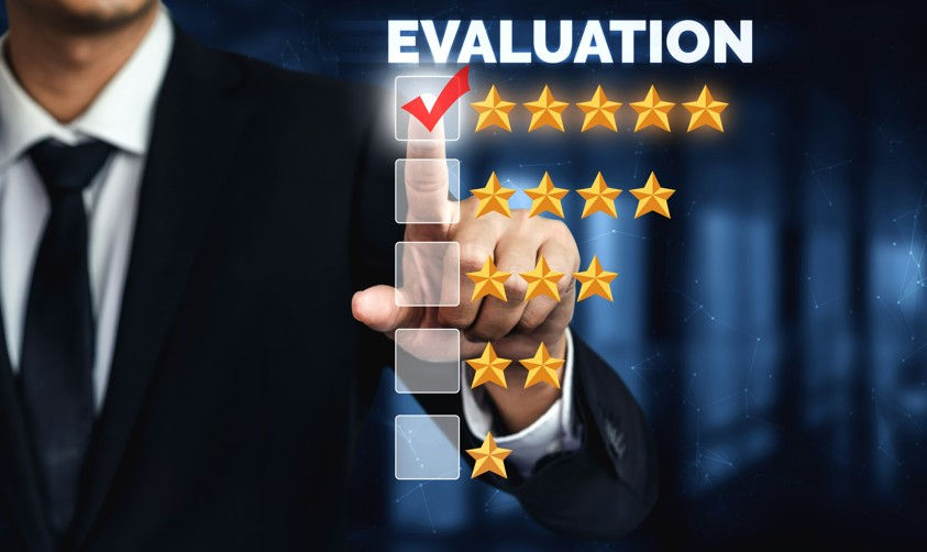 A person in a suit points at a virtual rating board with gold stars. "EVALUATION" text above, with a red check mark and a dark blue background.