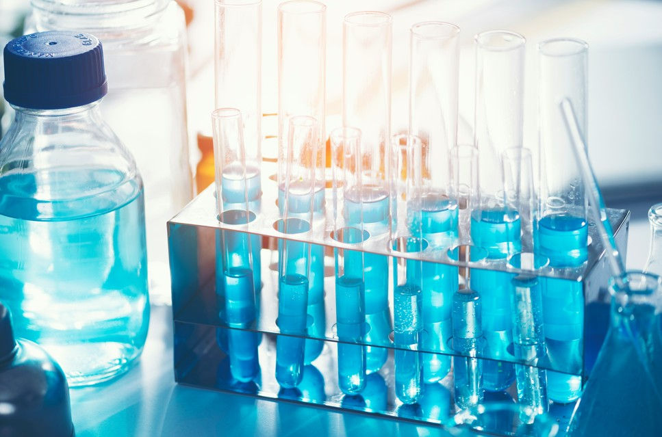 Blue liquid in test tubes and bottles on a lab bench, lit by bright light, creating a clean scientific mood.
