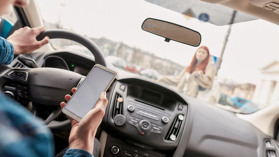 Driver using a phone at the wheel inside a car, with a woman crossing the street outside. Overcast day, urban setting, cautious mood.